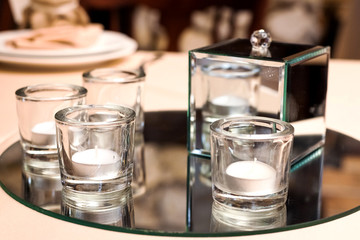 candles in glasses and a vitreous box standing on a round mirrored tray on a table at a wedding banquet