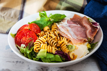 Salad with fusilli pasta accompanied tomatoes, mozzarella, smoked ham and italian cheese