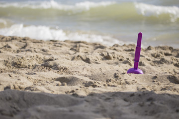 Fototapeta na wymiar closeup of purple beach scoop in the sand, game for child with sea in the background