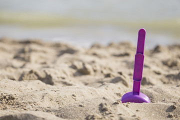 closeup of purple beach scoop in the sand, game for child with sea in the background