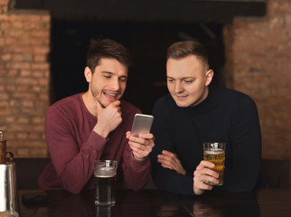 Friends enjoying fresh beer at pub and sharing mobile