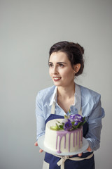 confectioner in a blue apron on a light background with a cake