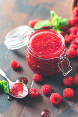 fresh raspberry jam in a glass jar on a wooden table, next to fresh raspberries and mint leaves. concept of homemade jam, preparation for winter,  selective focus and copy space