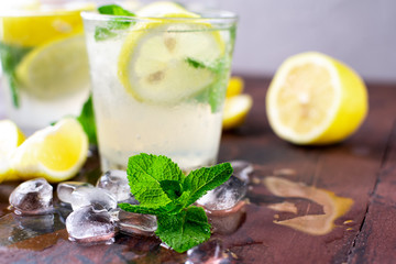 refreshing citrus lemonade with lemons, mint and ice in the bar, glass cups on the wooden table,...