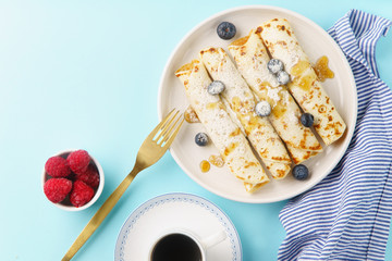 Rolled pancakes with blueberry and raspberry, caramel and powdered sugar on blue background. Top view