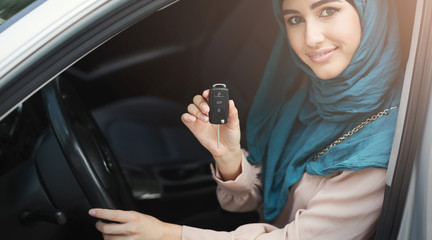 Happy arabian woman holding car key in new vehicle