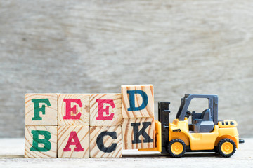Toy forklift hold letter block d,k to complete word feedback on wood background