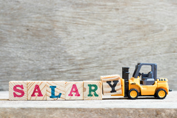 Toy forklift hold letter block y to complete word salary on wood background