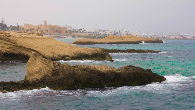 Rocks in waves and seashore with fortress (Ribat) in Monastir city, Tunisia