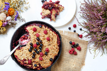 Berry crumble in the black cast-iron frying pan on the white table