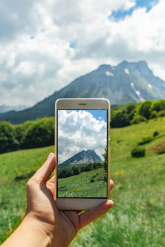 Female hand holding mobile phone and  
take a picture of mountain  