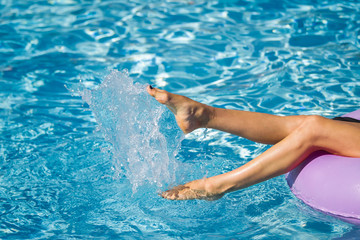 Womans legs on the inflatable ring playing with water in the swimming pool. Summer Vacation. Enjoying suntan. Weekend on resort