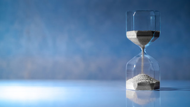 Sliver sand running through the shape of modern hourglass on white table.Time passing and running out of time. Urgency countdown timer for business deadline concept