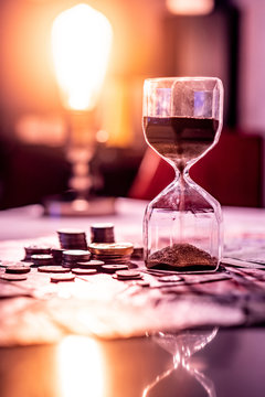 Sand running through the shape of hourglass on table with banknotes and coins of international currency. Time investment and retirement saving. Urgency countdown timer for business deadline concept