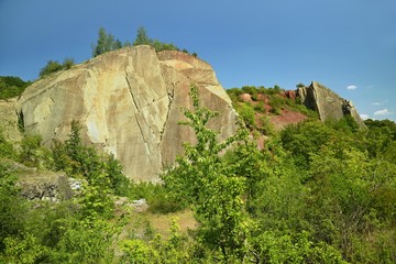 Big yellow and red perpendicular rocks standing in Hlubocepy, Prague, Europe, former limestone quarry, green trees and bushes, sunny summer day, blue sky