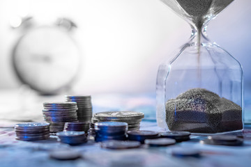 Sand running through the shape of hourglass on table with banknotes and coins of international...