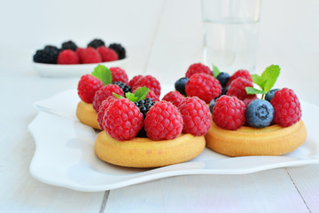 Soft sugar cookies topped with fresh forest fruits, raspberries, blackberries, blueberries on white plate
