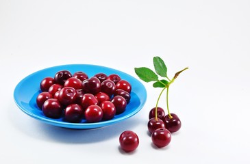 Ripe dark red cherry on the cuttings with leaves on a blue plate.