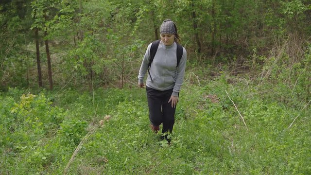 woman with a backpack rises a hill in the forest.