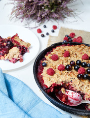 Berry crumble in the black cast-iron frying pan on the white table