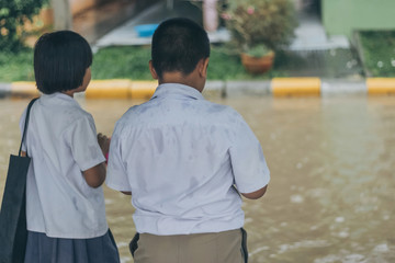 Boy and girl  wait to cross flooded street in heavy rainstorm be