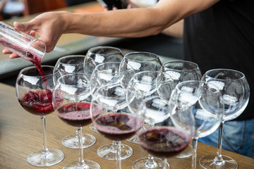 Pouring red wine from decanter into the wineglass on row of glasses. Close up of red wine to service winery to party or event.