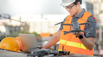 Young Asian engineer man working with drone laptop and smartphone at construction site. Using...