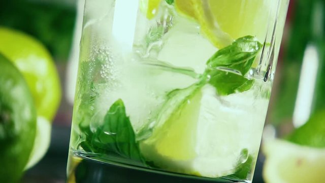 Slow motion vodka pour into a glass of ice with citrus and mint at an angle