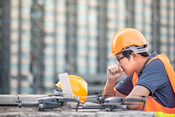 Young Asian engineer man working with drone laptop and smartphone at construction site. Using...