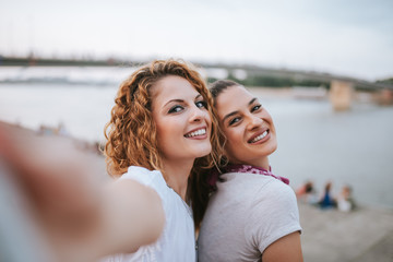 Obraz premium Close-up image of two girlfriend making selfie near the river in the city.