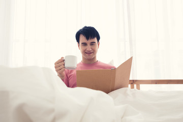 Man drink coffee In bed whilst read  book.