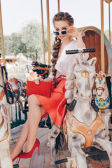 Close up Portrait of a Happy Pretty Lady Standing in Front of the Carousel at the Park. Retro Style of Dress and Fashionable Make Up and Hair. Film Toning and Color