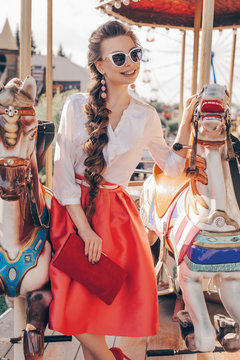 Close up Portrait of a Happy Pretty Lady Standing in Front of the Carousel at the Park. Retro Style of Dress and Fashionable Make Up and Hair. Film Toning and Color