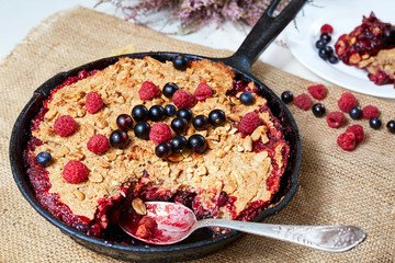 Berry crumble in the black cast-iron frying pan on the white table
