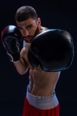 Fototapeta na wymiar Portrait of tough male boxer posing in boxing stance against black background.