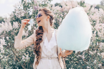 Portrait of a Smiling Beautiful Lady in Sunglasses Holding Cotton Candy at Park and Happily Looking...