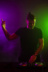 DJ playing music at mixer on colorful foggy background