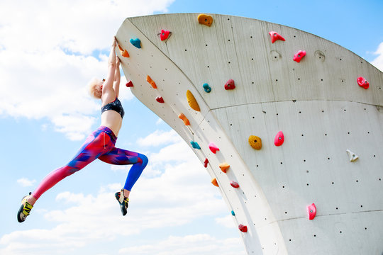 Photo from below of sports woman in leggings hanging on wall for climbing against blue sky