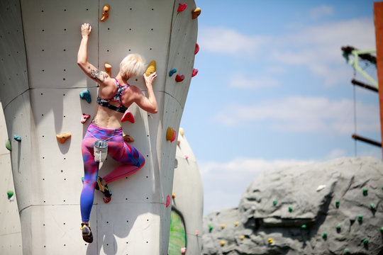 Photo from back of sportswoman with short haircut in sportswear on workout at wall for rock climbing