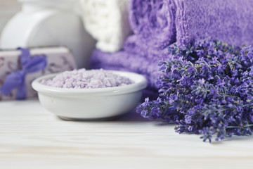 Obraz na płótnie Canvas Lavender flowers, lavender soap, aromatic sea salt and towels. Concept for spa, beauty and health salon, cosmetics store. Close up photo on white wooden background.