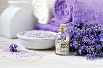 Fototapeta na wymiar Lavender flowers, aromatic sea salt and towels. Concept for spa, beauty and health salon, cosmetics store. Close up photo on white wooden background.