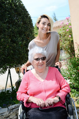 cheerful old woman in a wheelchair with her young granddaughter outdoor in hospital