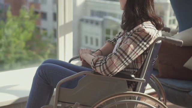 Disabled girl sitting by the window in a wheelchair.Slow mo