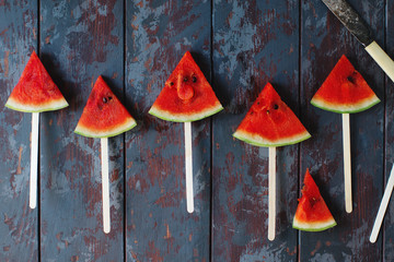 Fresh organic watermelon slice popsicles on a dark rustic wooden background. Top view, selective focus. Tasty summer fruit, healthy lifestyle