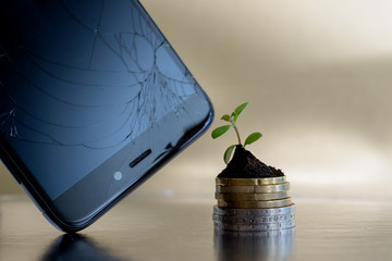 Broken phone display and golden and silver coins in soil with young plant. Repair phones business concept