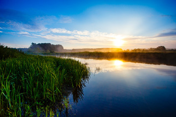 Bright sunrise and blue sky over foggy river in the countryside