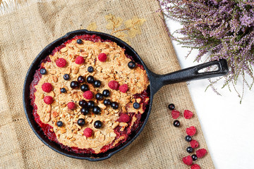 Berry crumble in the black cast-iron frying pan on the white table