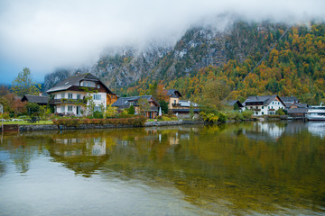 Fototapeta na wymiar Wonderful view of small village with houses on calm lake and fog mountains on background. Autumn in Hallstatt, Austria