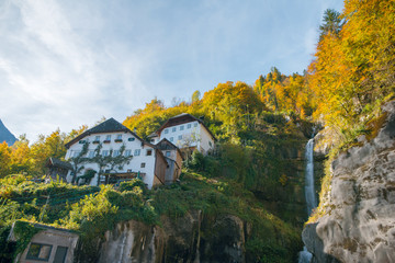 Fototapeta na wymiar Beautiful view of houses on the green mountain hills and waterfall. Sunny Autumn day. Countryside. Hallstatt, Austria