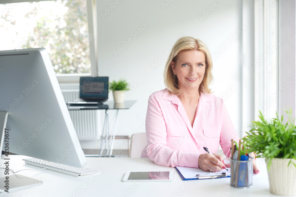 Wall mural Successful senior businesswoman writing something while sitting at office desk